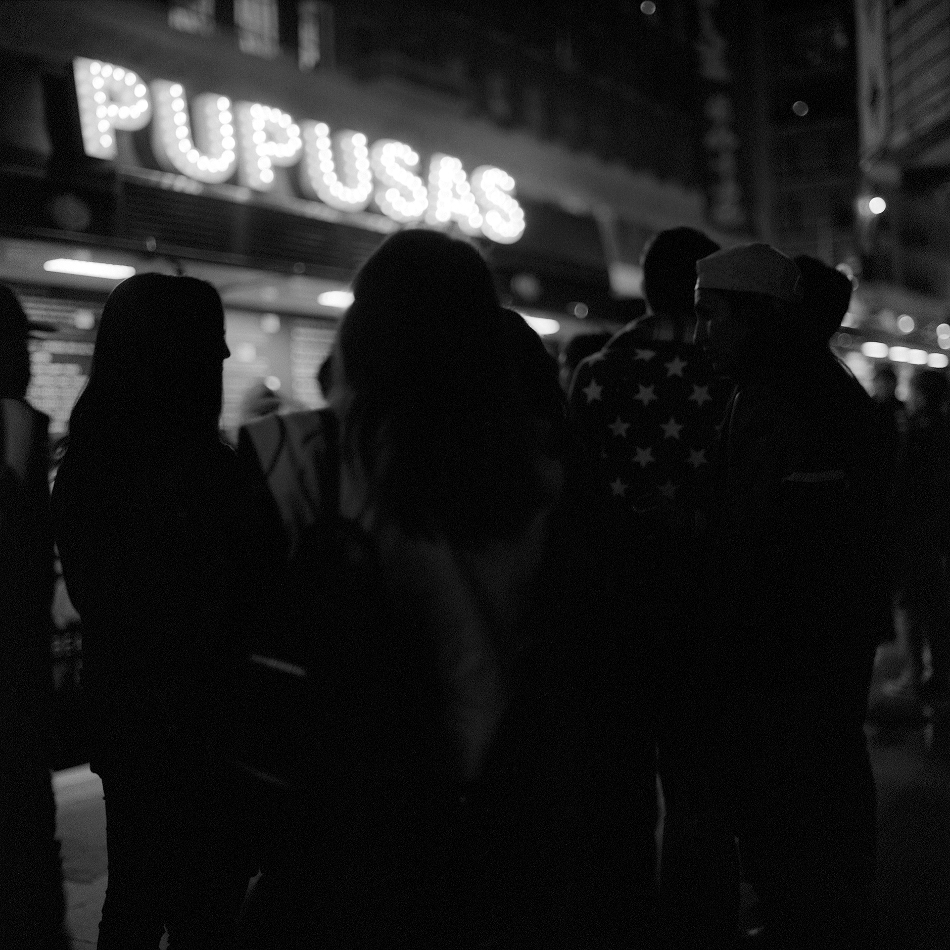 Silhouettes of people gathering to get pupusas from a food truck