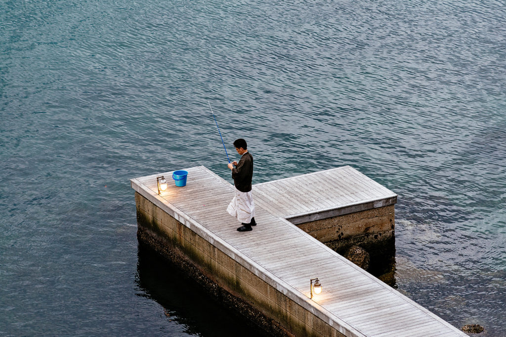A man prepares a fishing rod on a dock near an Awajishima resort